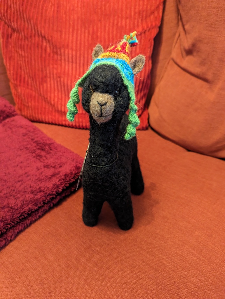 A black alpaca stuffed animal with a colorful Peruvian hat on its head sits on a red couch.